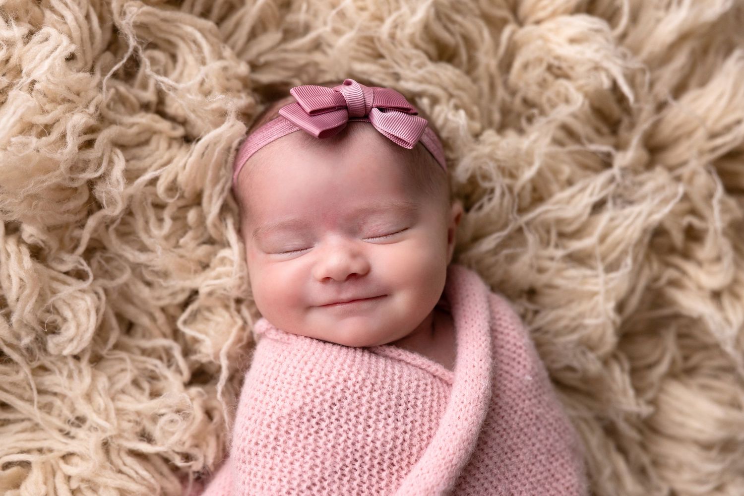 Newborn photography with pink wrap and bow on textured beige background.