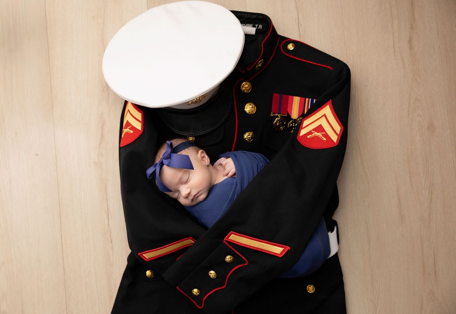 Newborn portrait nestled in military dress uniform with white cap.