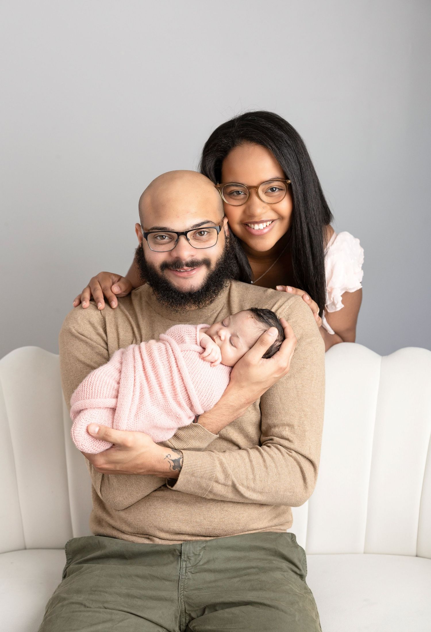 Intimate family moments captured on a white sofa against a minimalist gray backdrop.