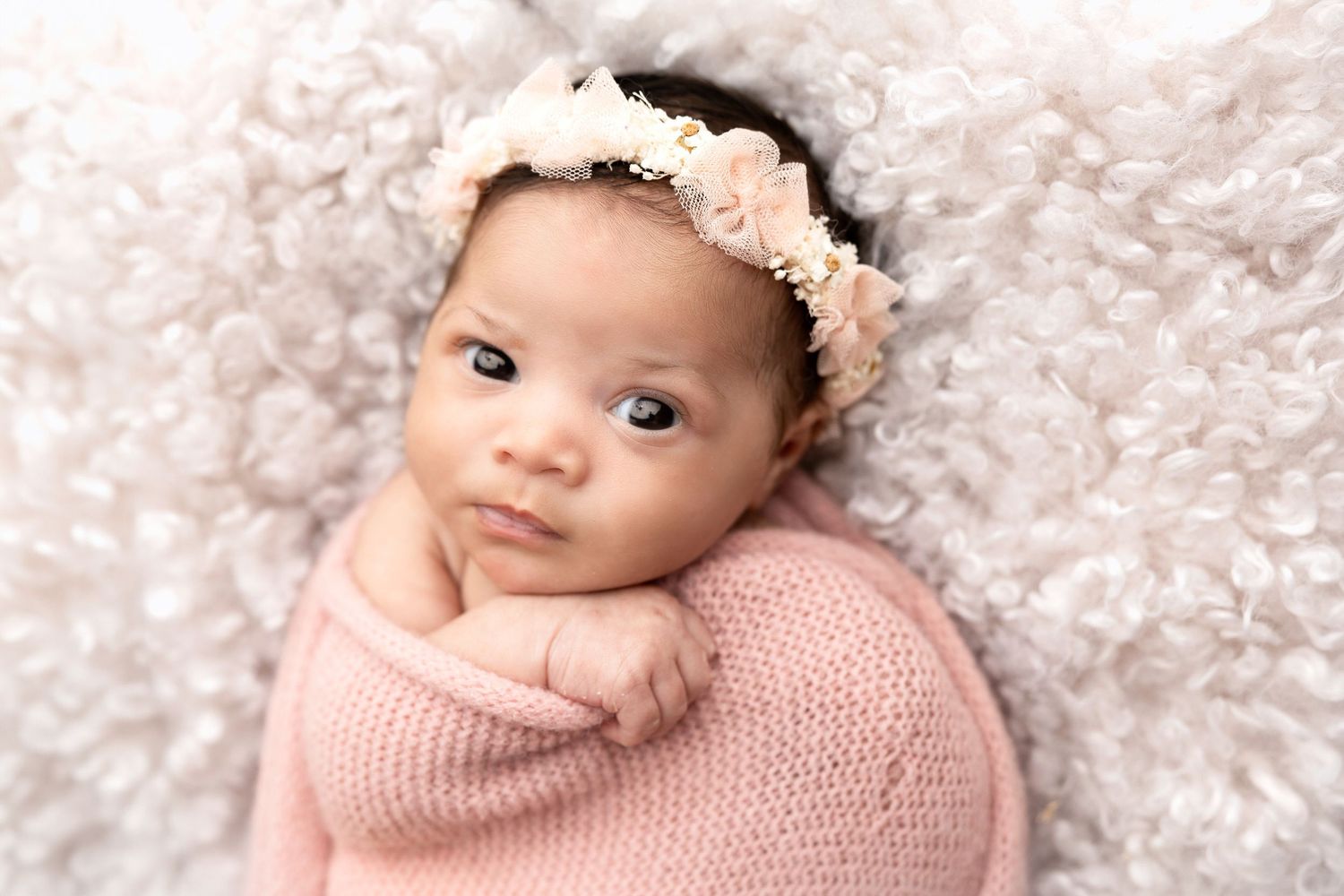 Newborn photography series featuring soft pink tones and delicate floral headpiece against textured background.