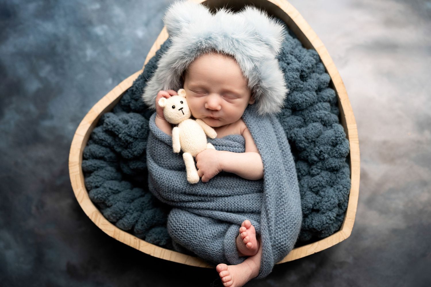 Sleeping newborn wrapped in grey blanket on textured backdrop.