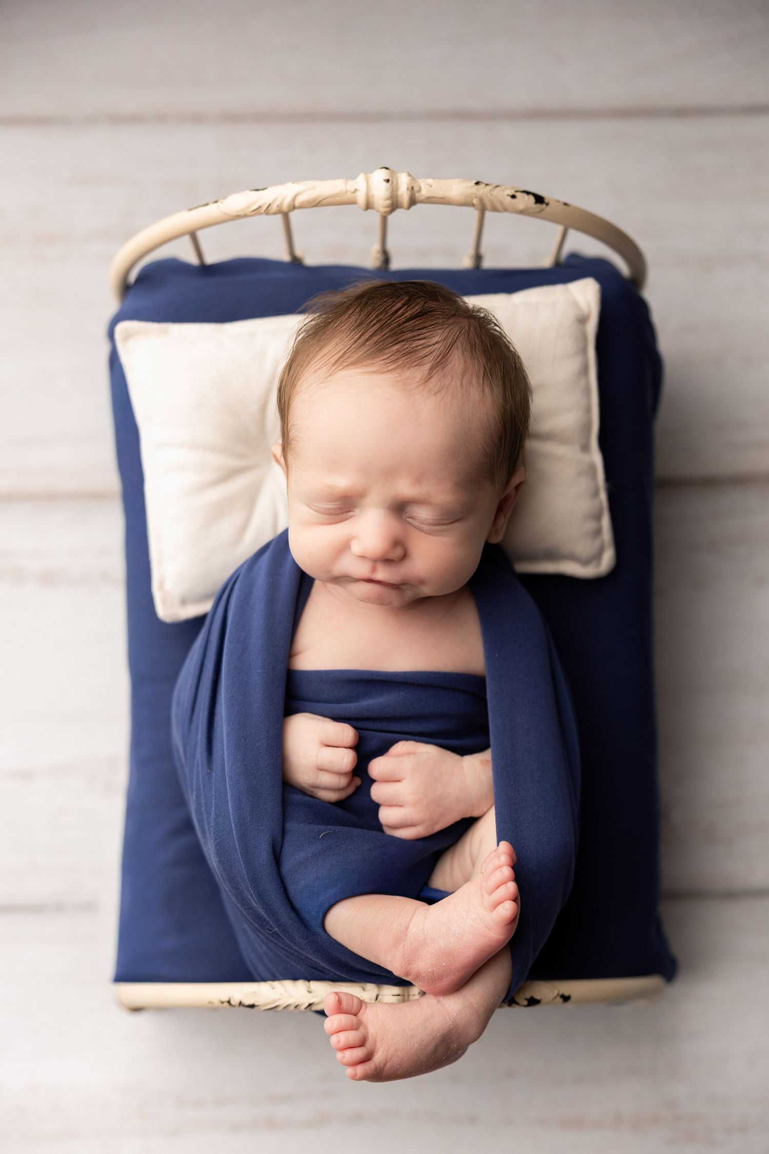 Newborn baby sleeping peacefully on navy and cream cushions.