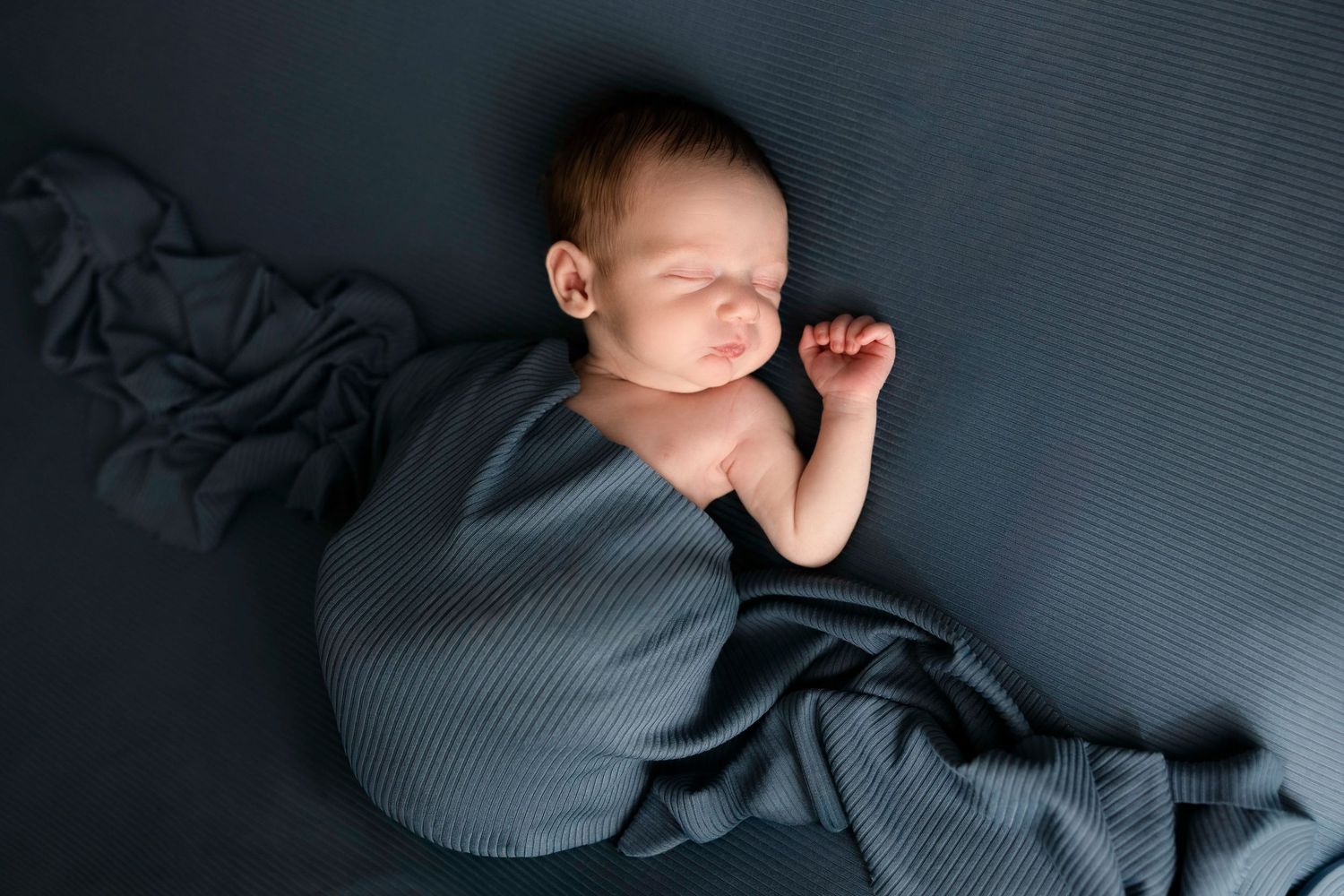 Artistic black and white portrait of sleeping newborn on textured surface.