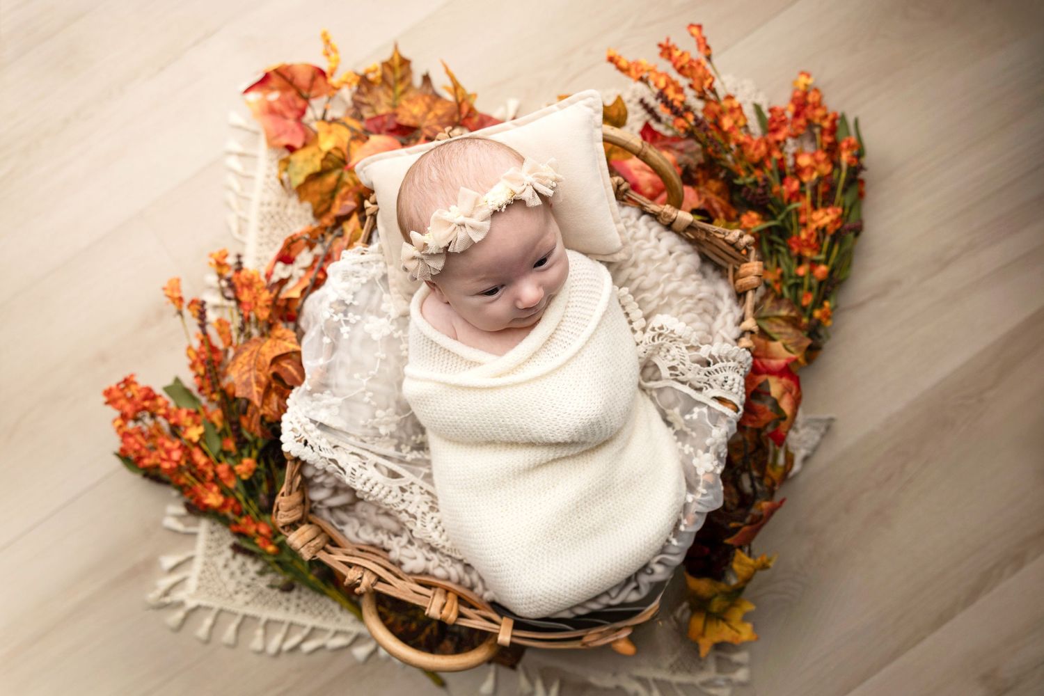Newborn photography setup with autumn decorations and white fabric.