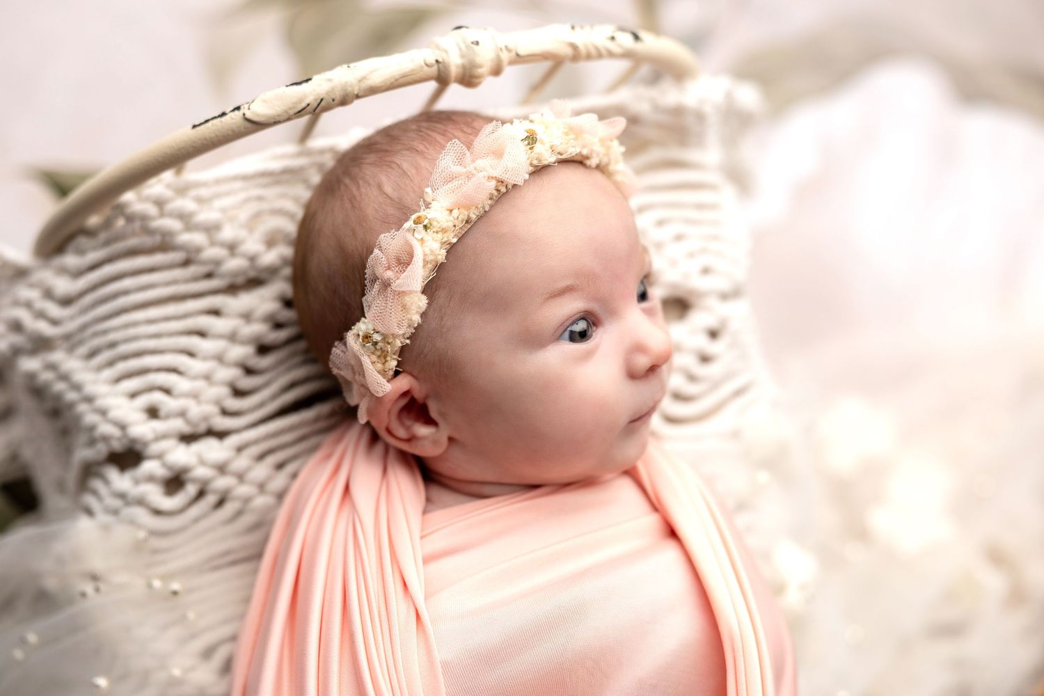 Delicate newborn portrait with soft pink headband and lace details.
