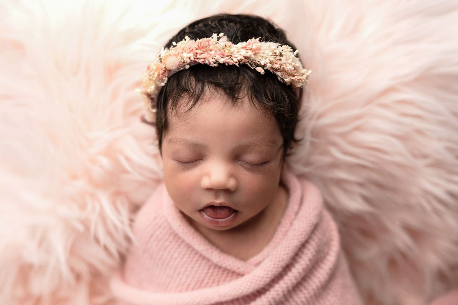 Delicate newborn photography session featuring soft pink tones and gentle wrapping.