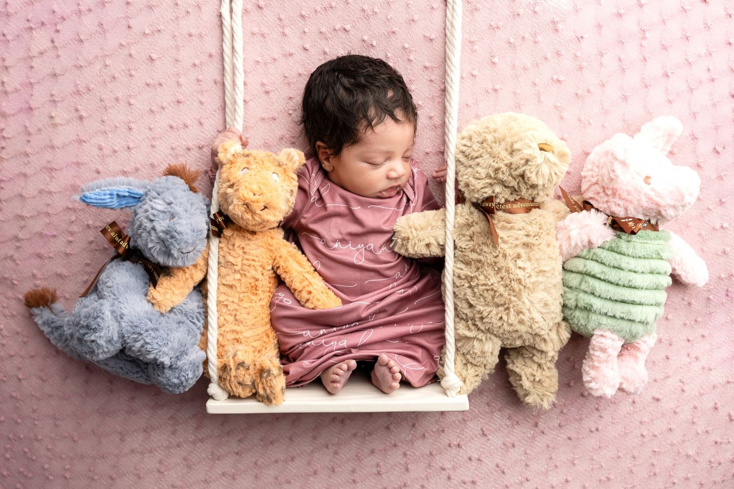 Sleeping newborn posed with plush teddy bears on pink backdrop.