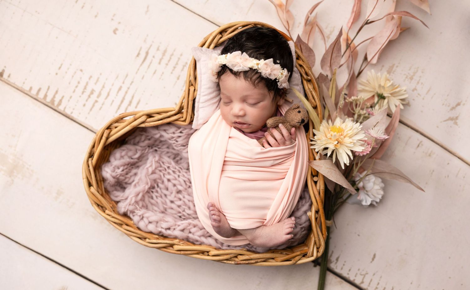 Newborn photography featuring wicker baskets and soft pink styling.