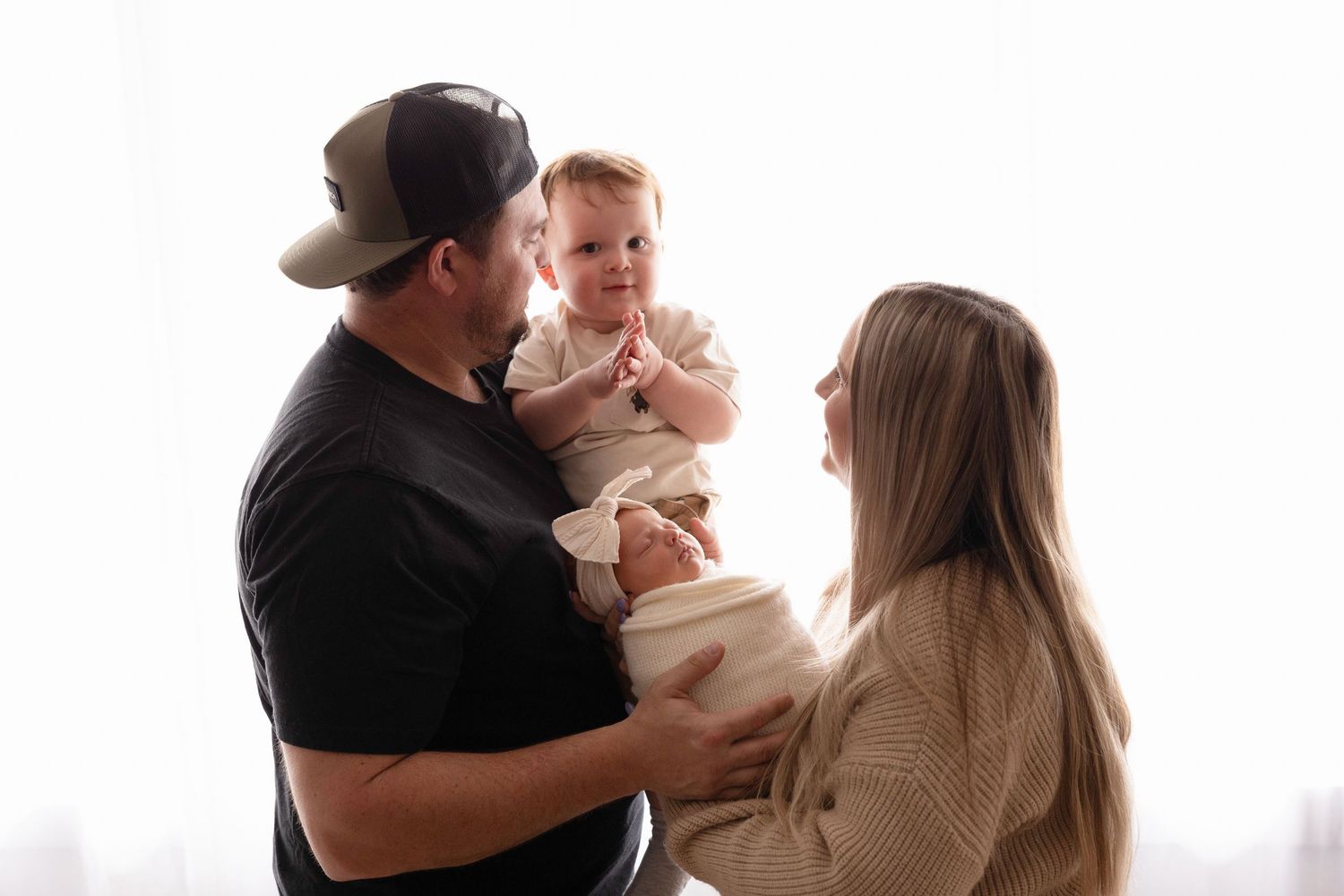Happy young family with mother and father holding adorable baby together in bright white studio.