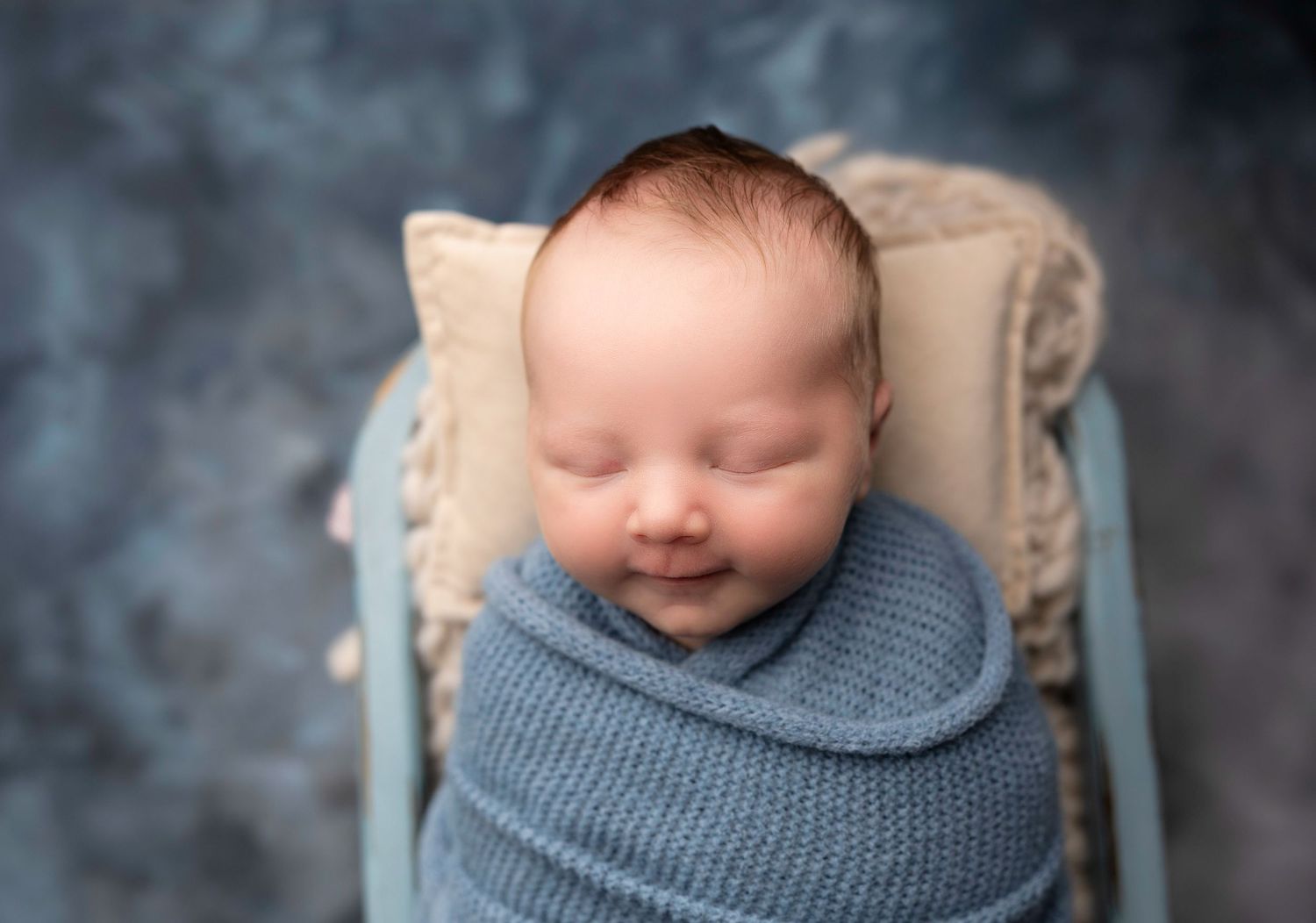 Newborn baby sleeping peacefully wrapped in blue knit blanket.