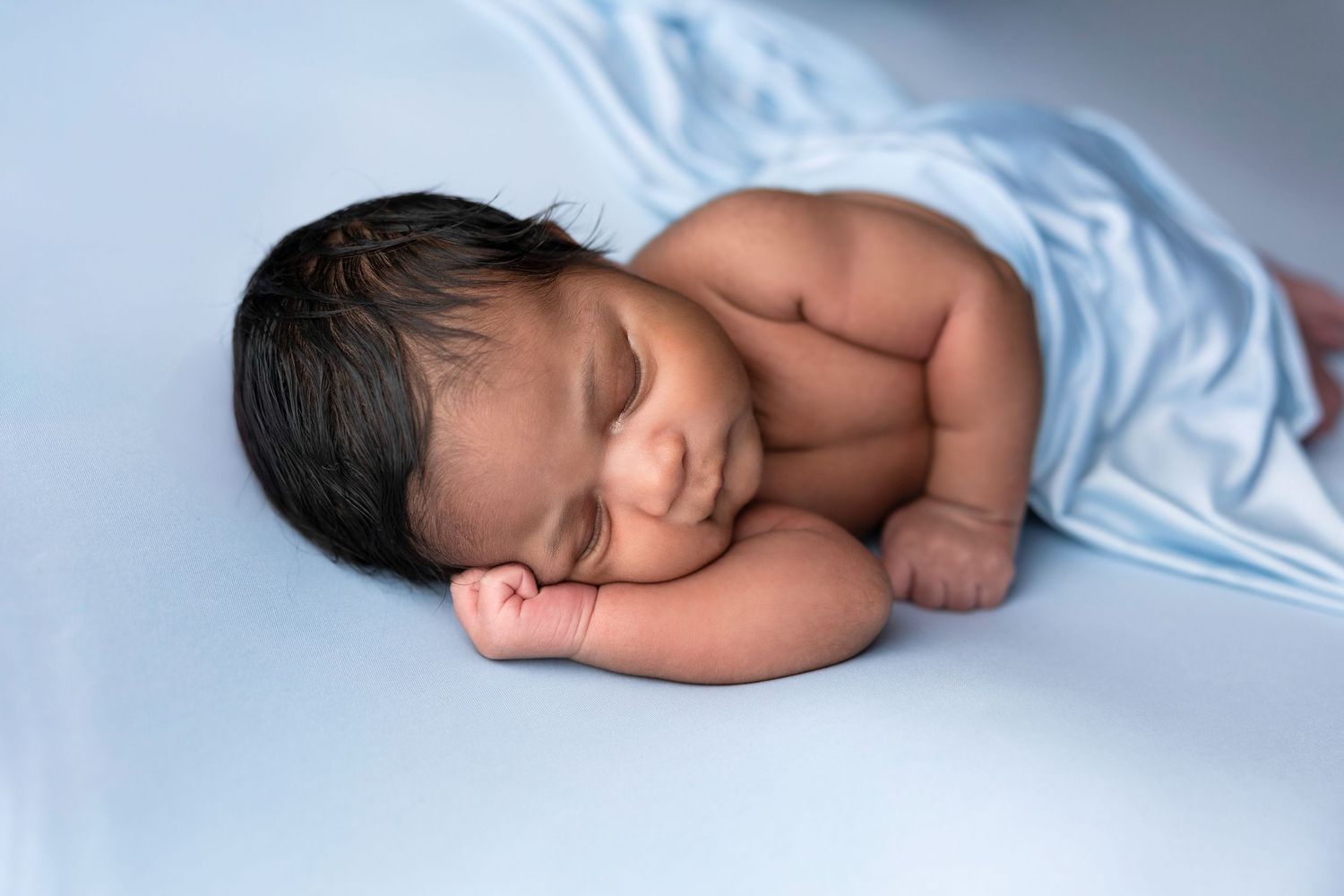 A minimalist newborn portrait on light blue background with gentle lighting.