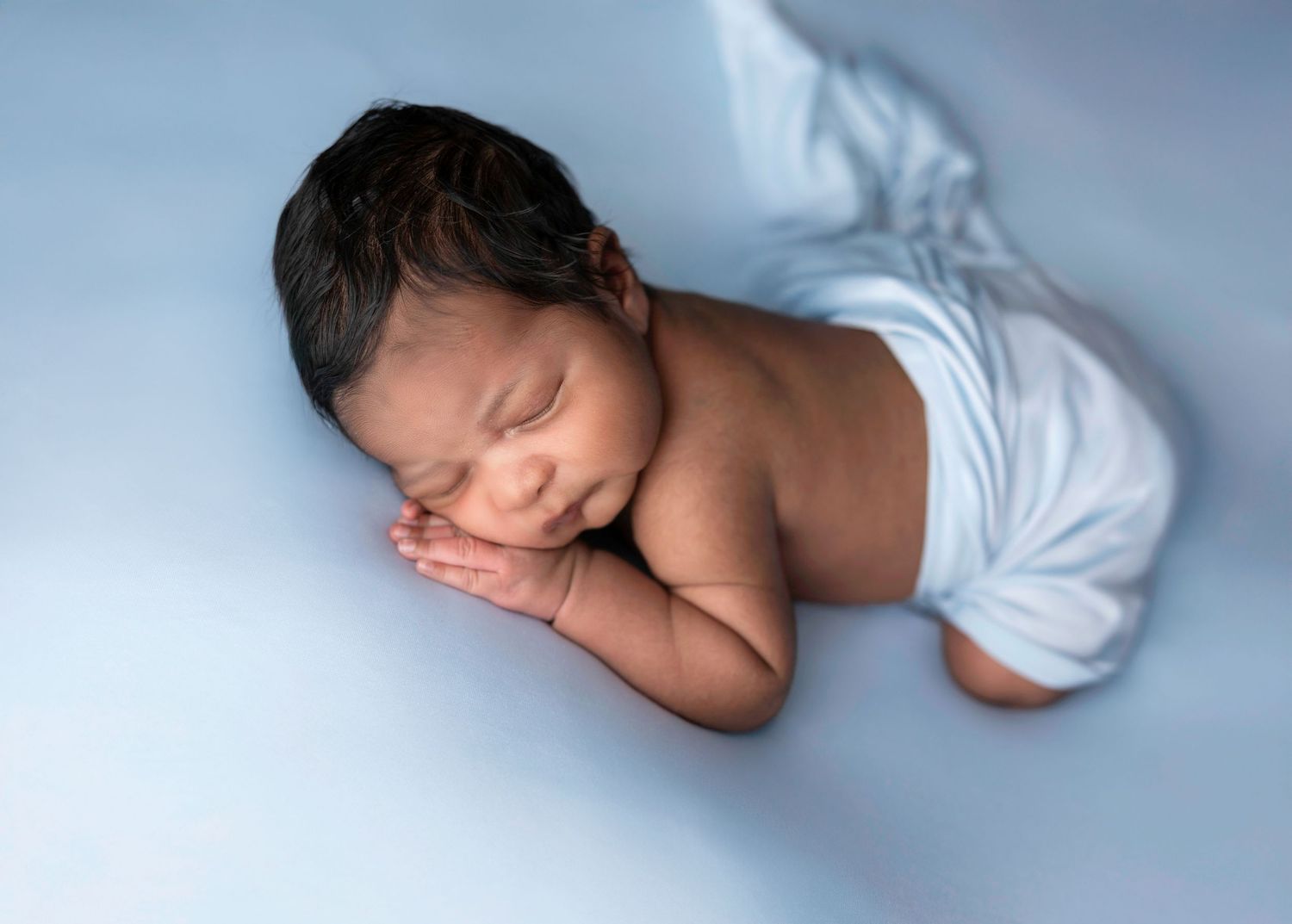 Artistic series of newborn photography poses in soft blue lighting against white background.