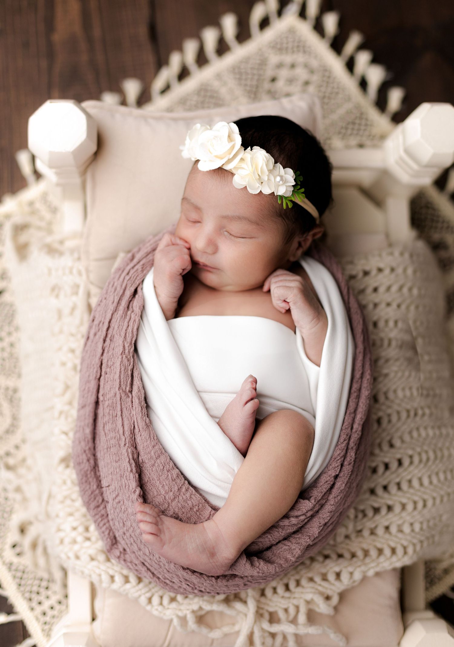 Peaceful newborn sleeping in vintage chair wrapped in mauve swaddle with delicate lace details.