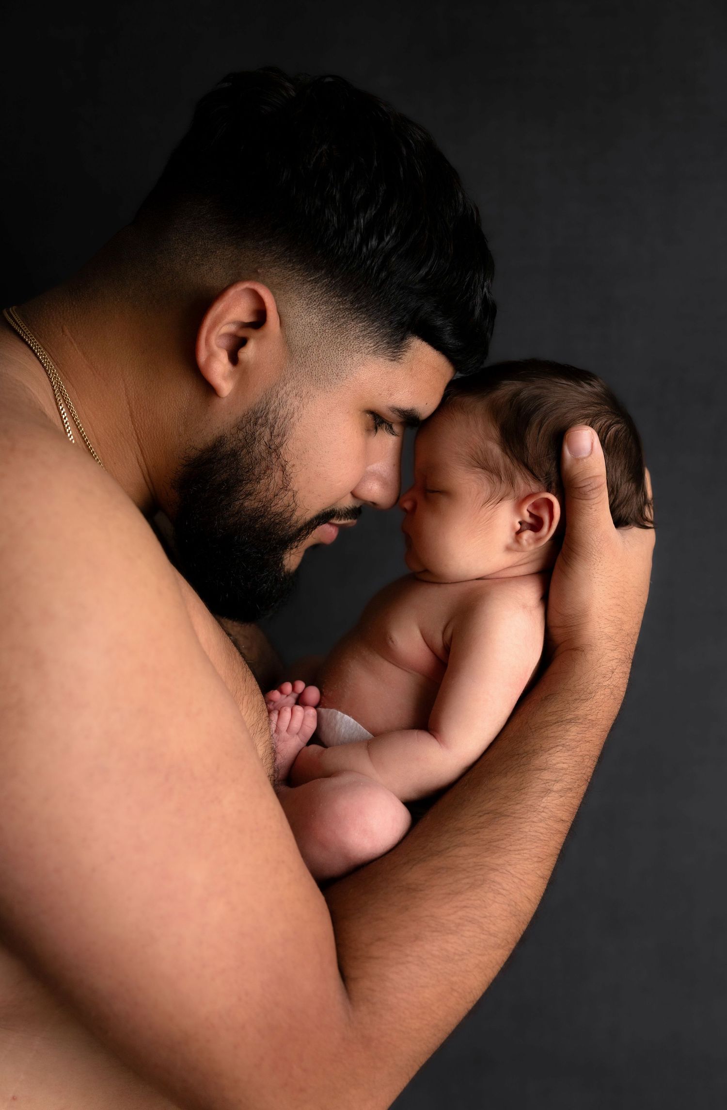 Tender black and white portraits showing parent cradling newborn against dark backdrop.
