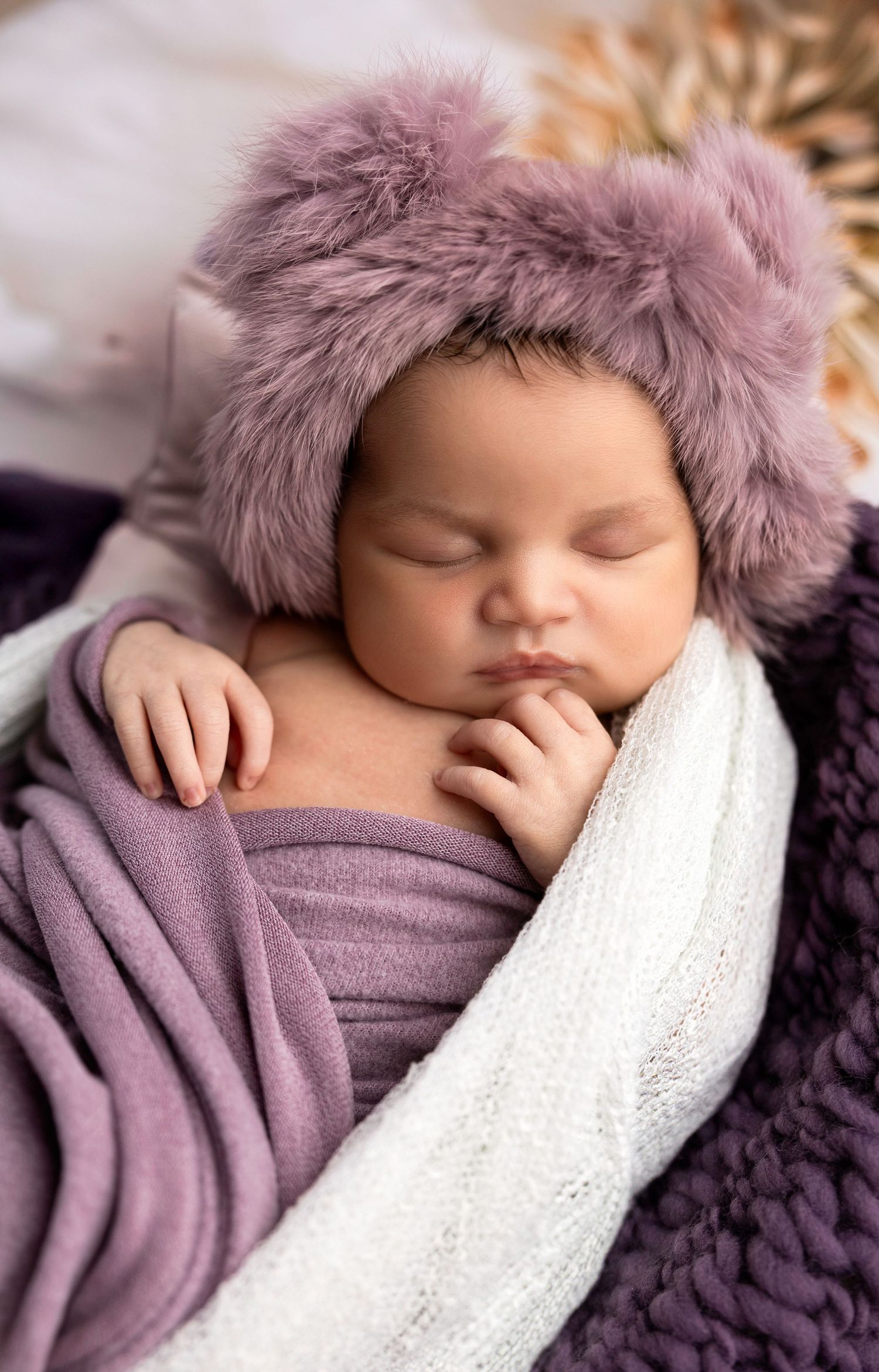Sleeping baby wrapped in purple fabric with white lace and furry hat details.