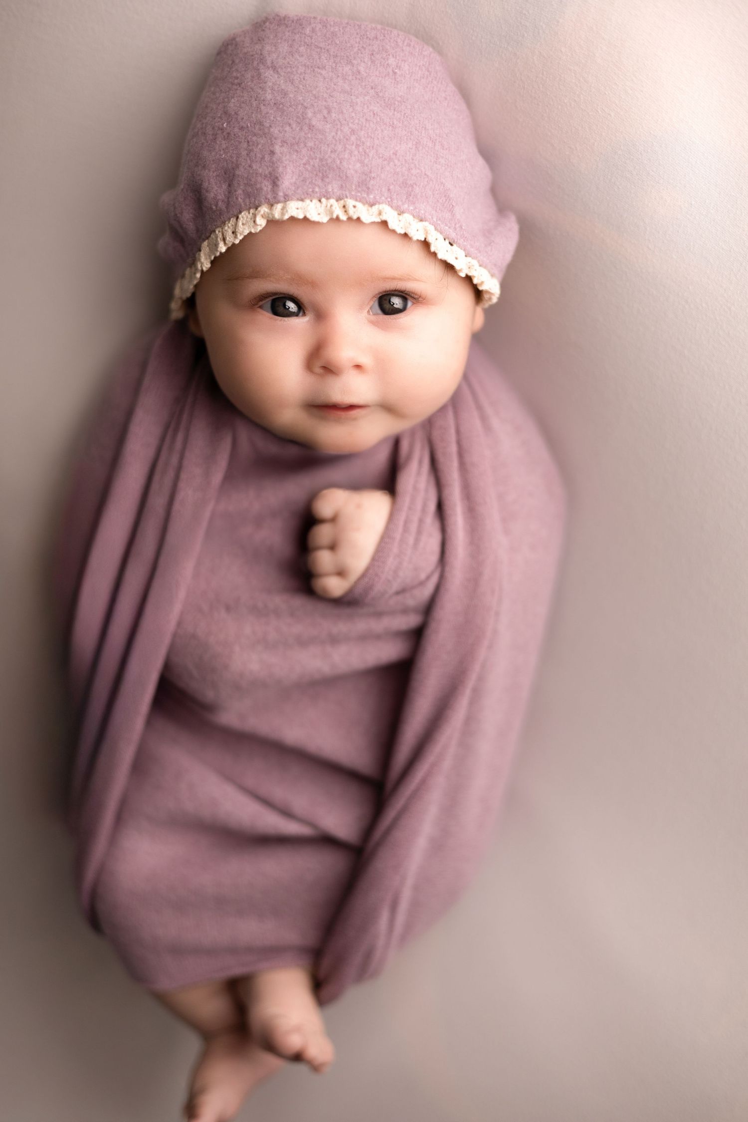 Newborn baby wearing soft pink outfit and bonnet on neutral background.