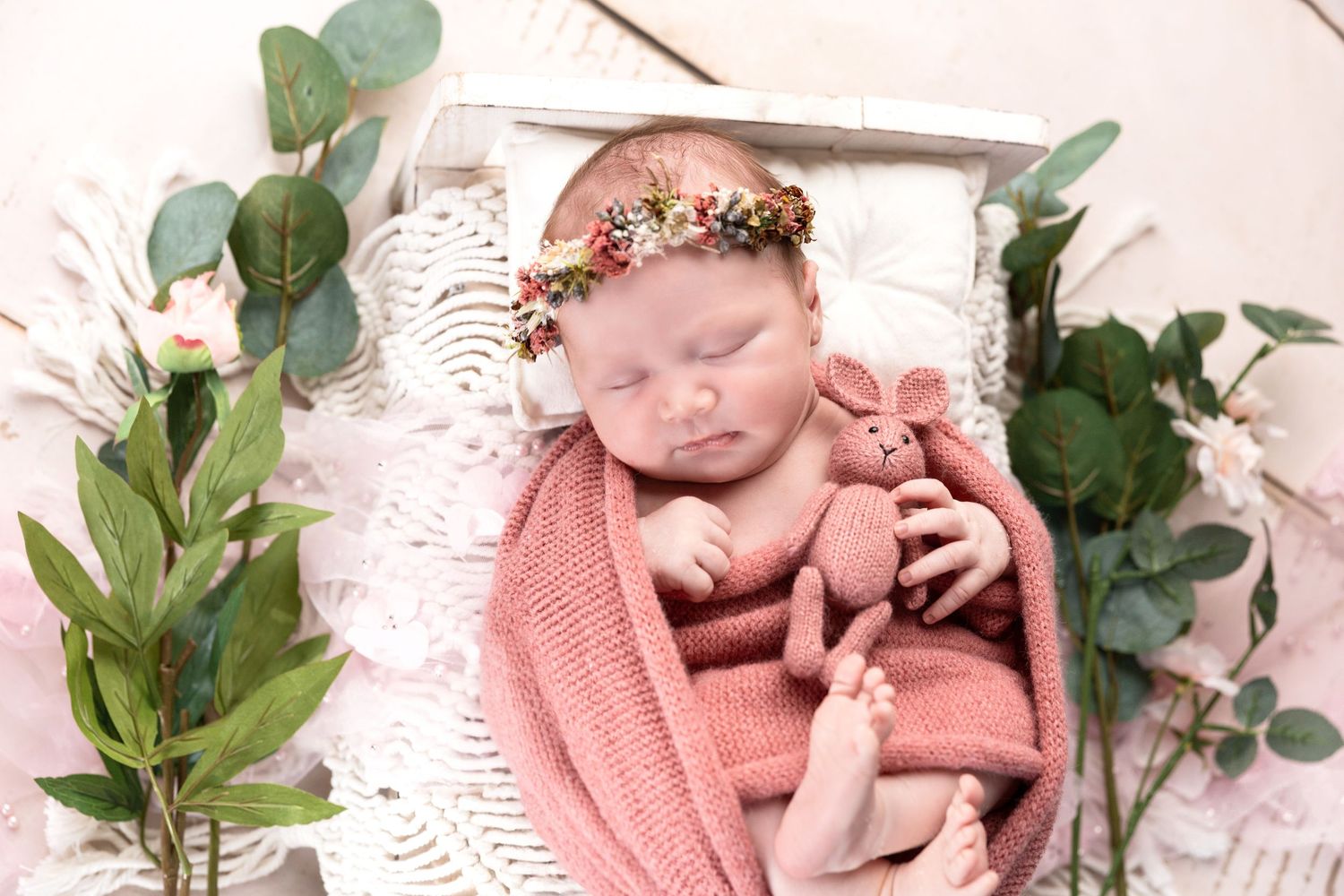 Newborn photo setup with pink blanket and decorative green eucalyptus leaves.