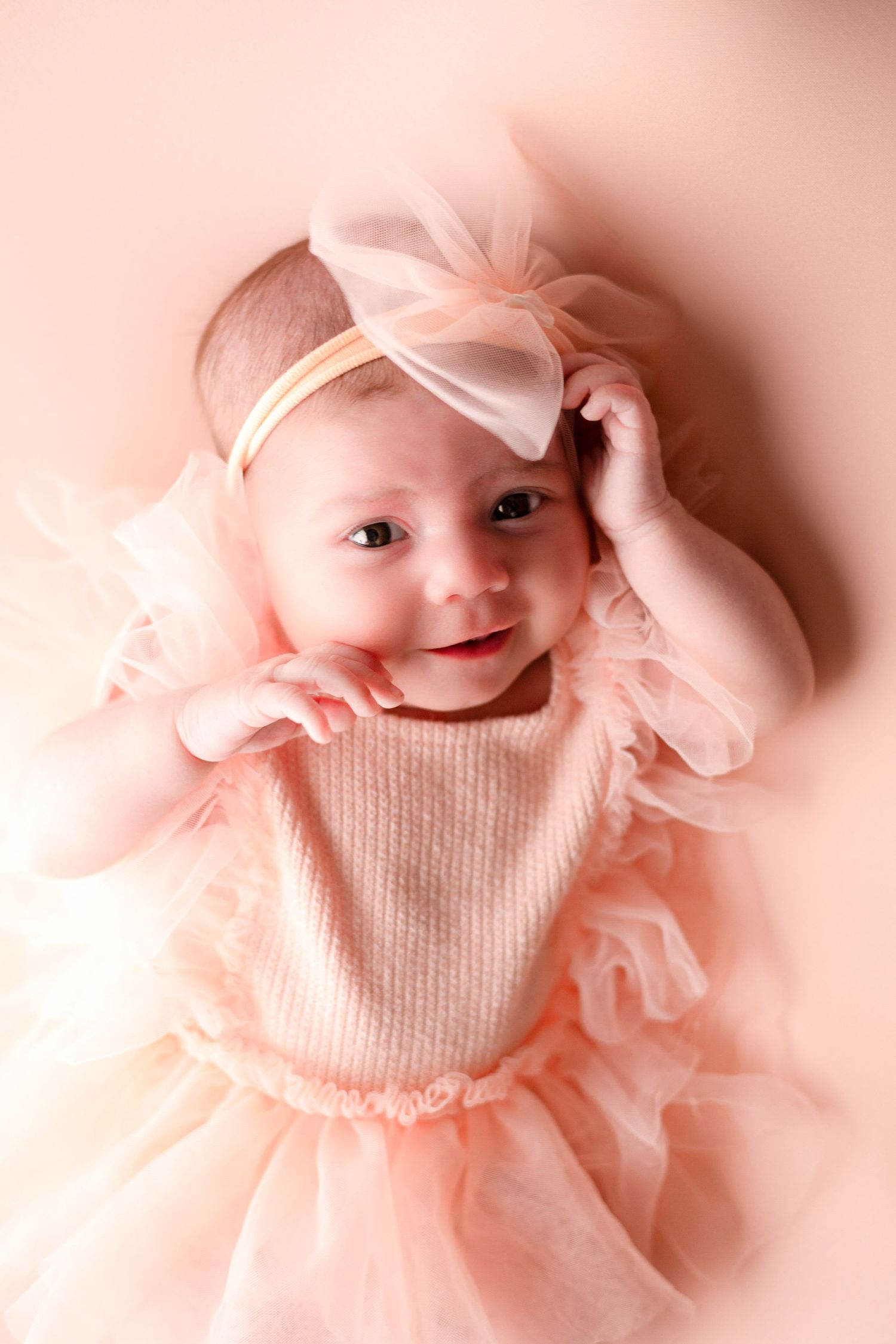 Baby in pink tulle dress and bow posing for portrait series.