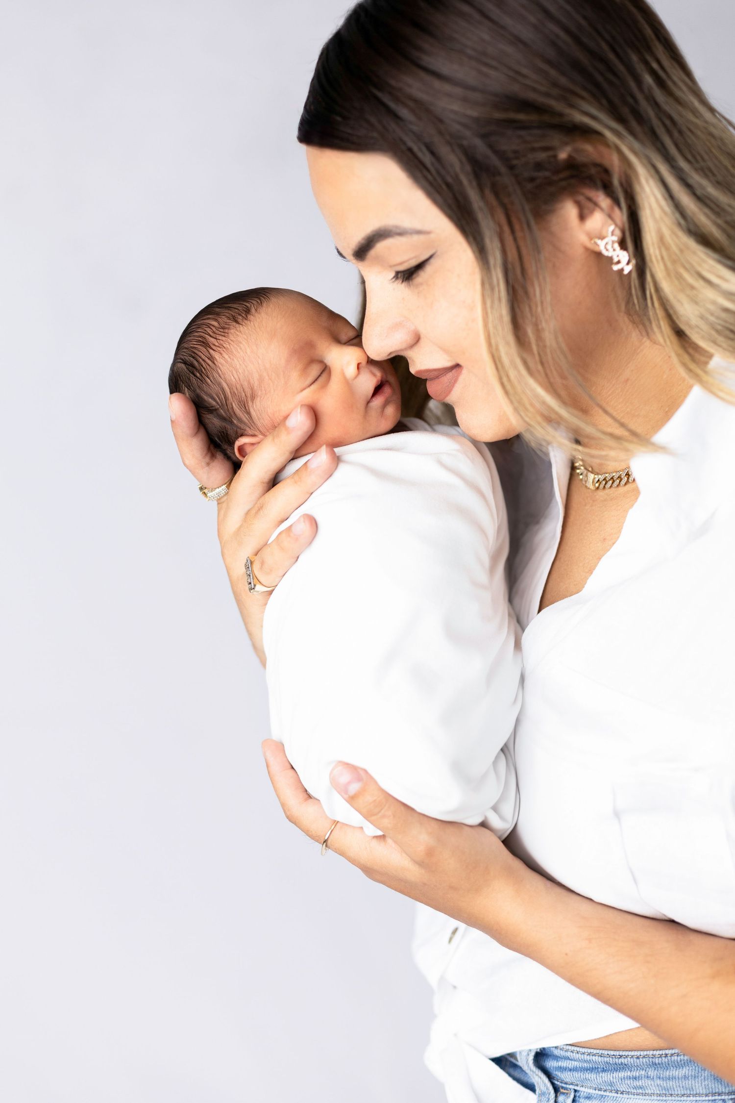 An intimate portrait of a woman in white holding and nuzzling a swaddled newborn baby.