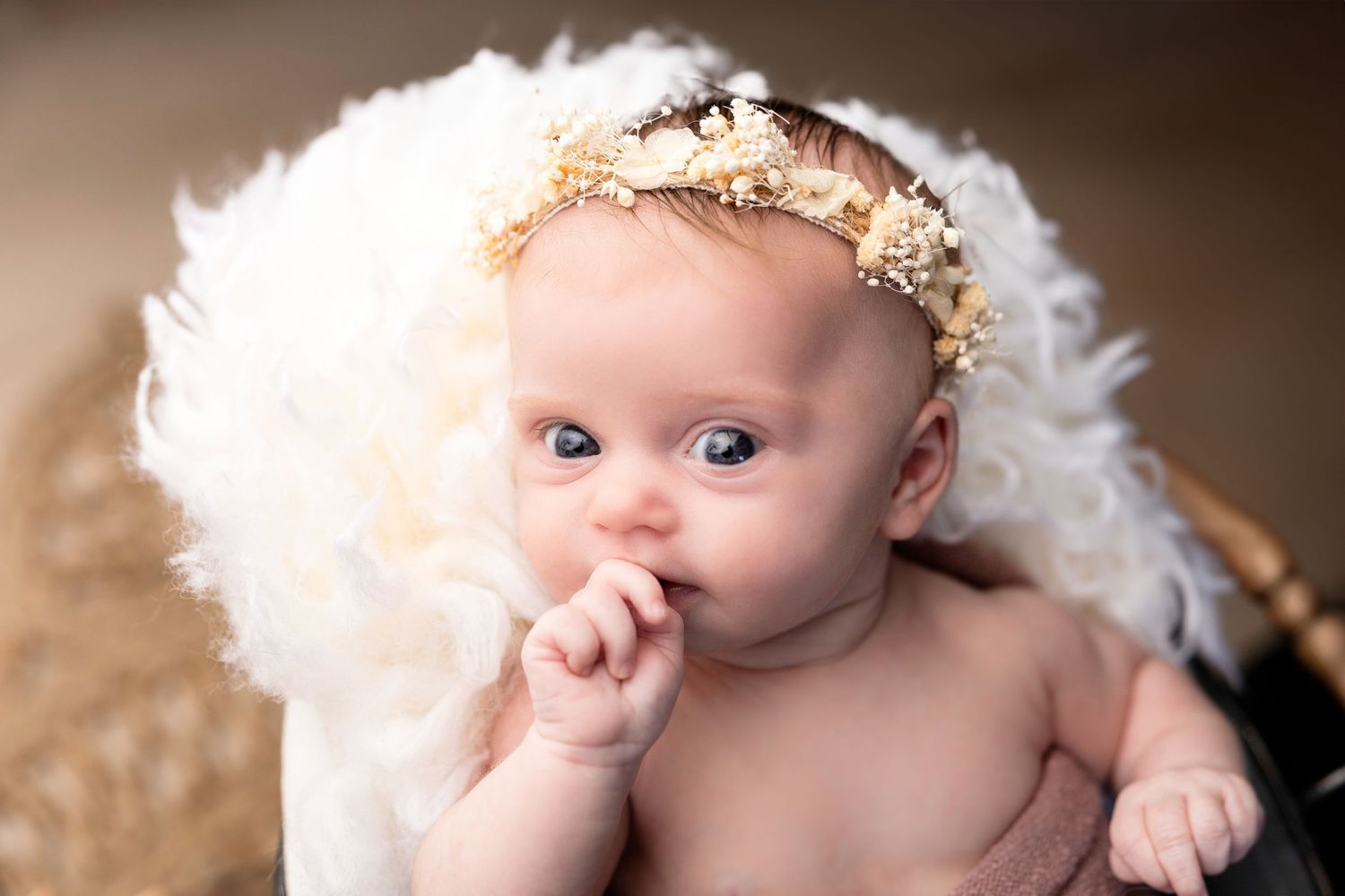 Newborn baby wrapped in white feathery blanket with delicate details.