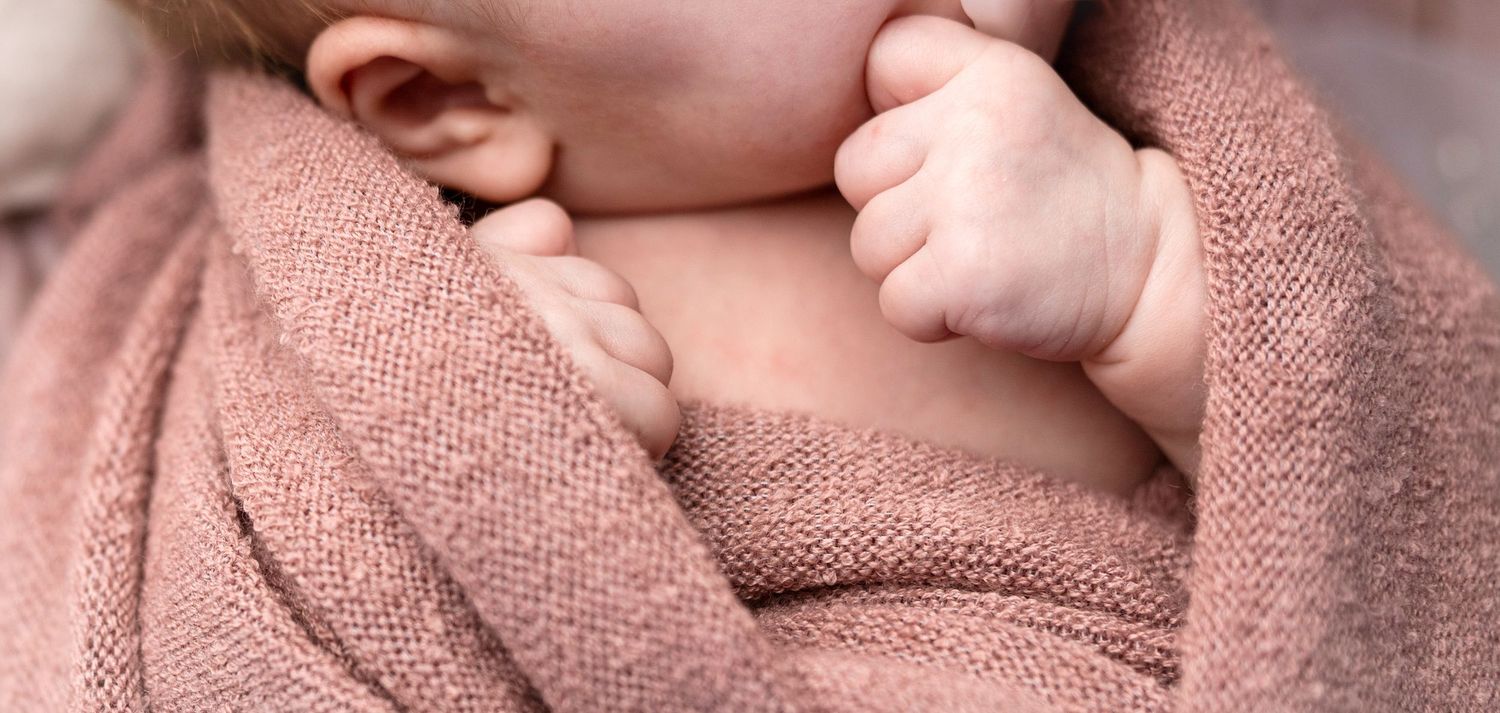 Close-up details of newborn baby wrapped in pink soft fabric.
