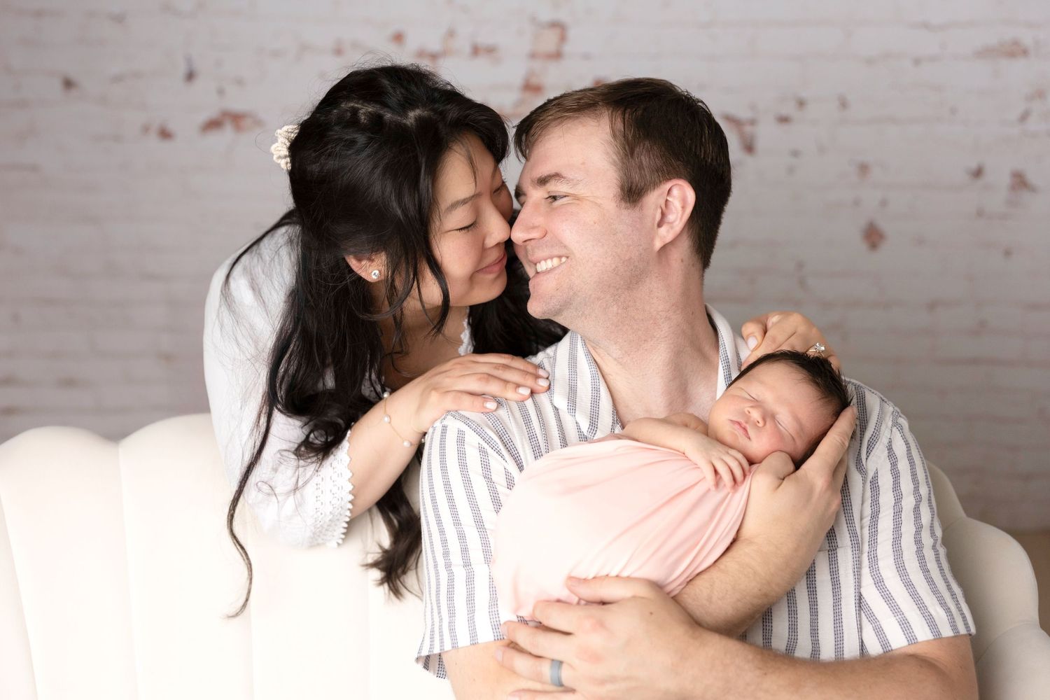 Intimate family portrait series against white brick wall showing affectionate moments.