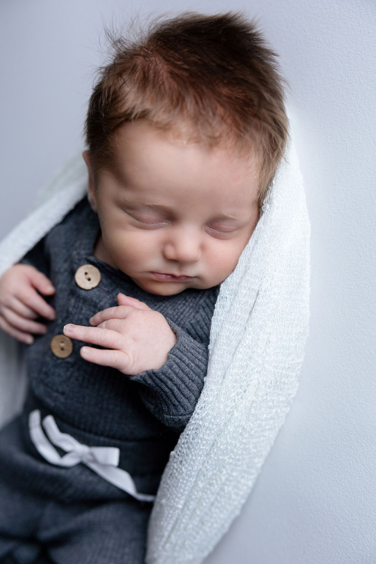 Sleeping newborn in grey outfit captured in soft focus against white background.