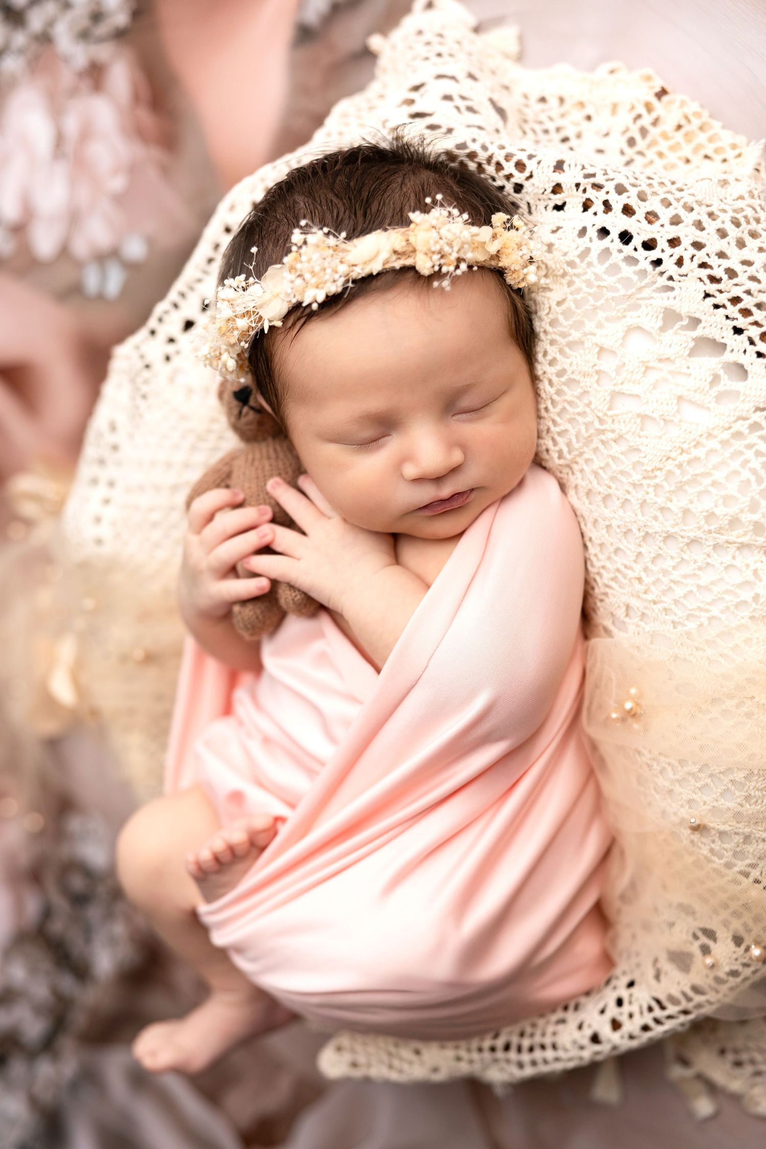 Sleeping newborn wrapped in pink fabric and vintage lace in dreamy portrait series.