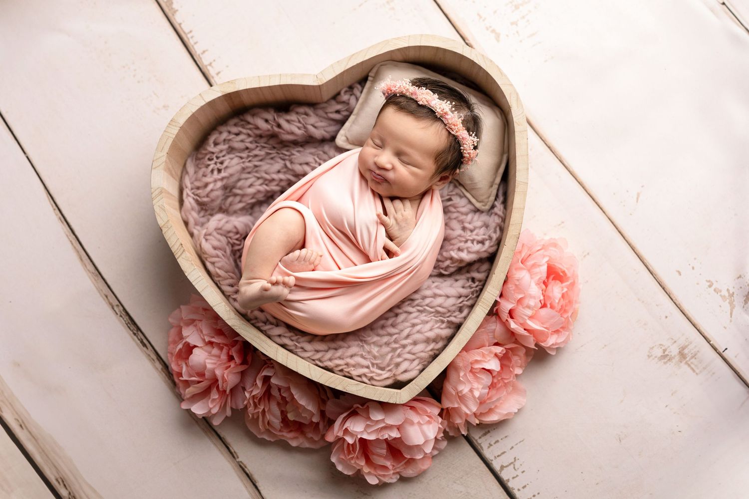 Newborn photography series with baby in pink wrap on rustic wooden backdrop.