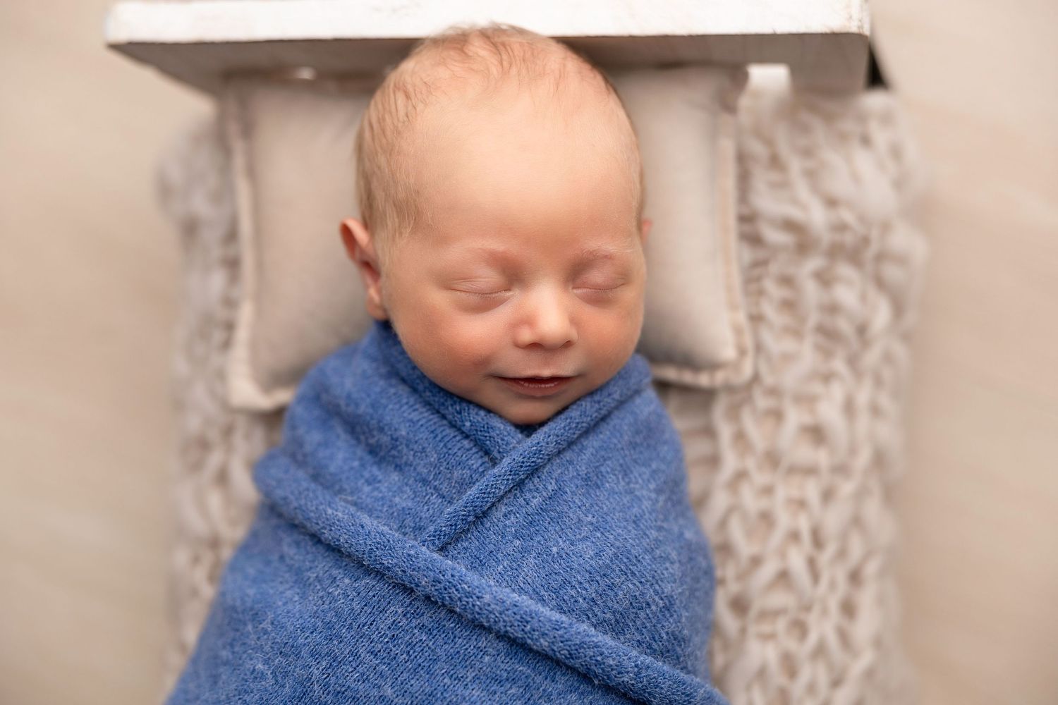 Sleeping newborn wrapped in soft blue blanket during professional photo session.