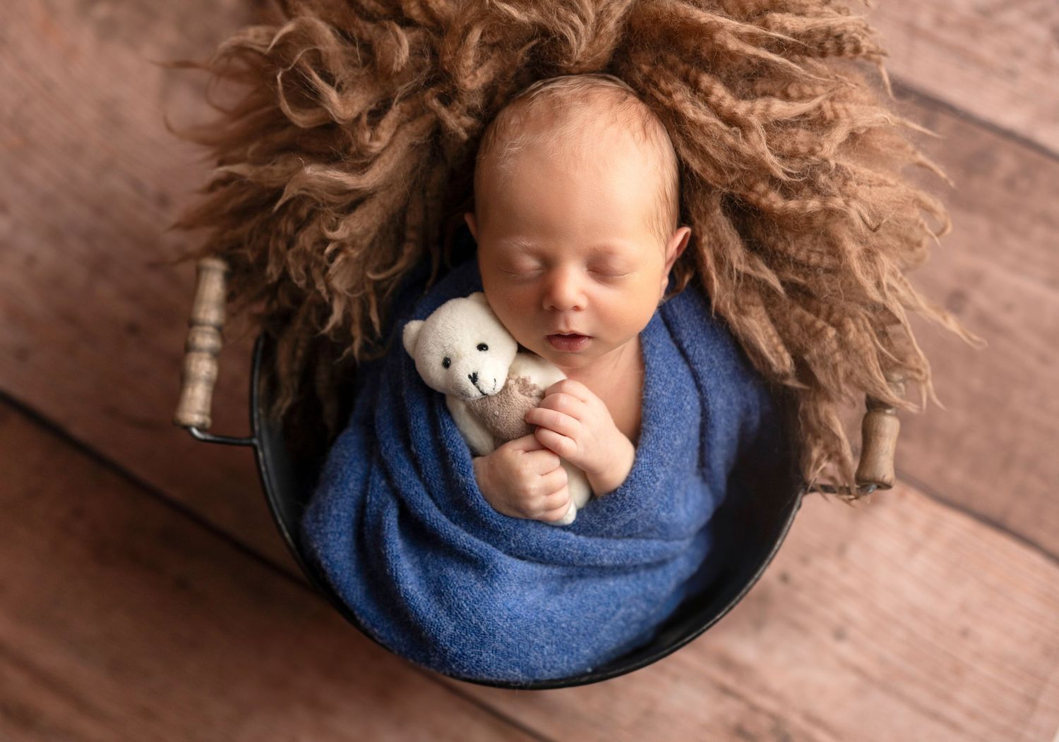Newborn sleeping peacefully on wooden surface with fluffy brown backdrop.