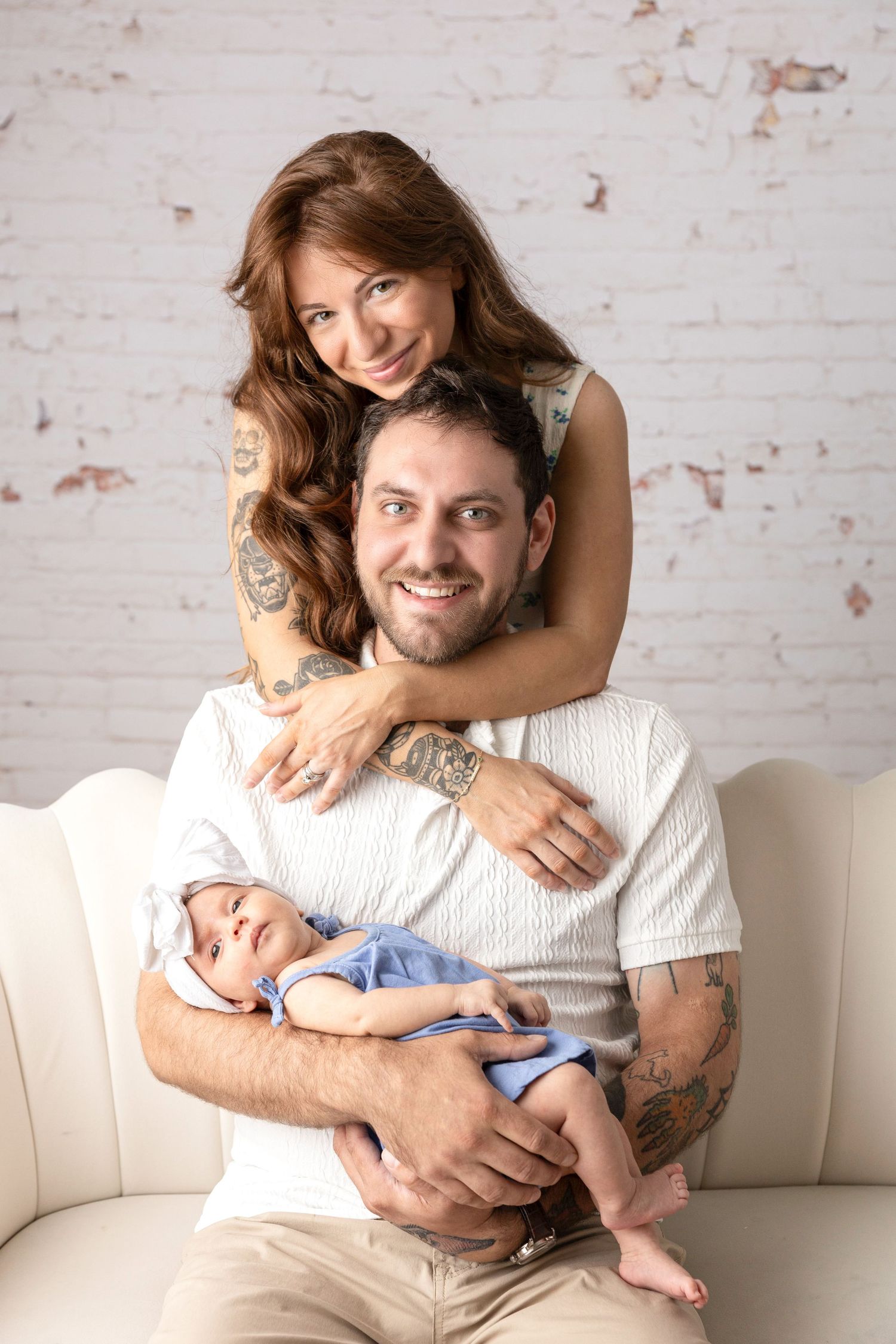 Loving family portrait on white couch against brick wall background.