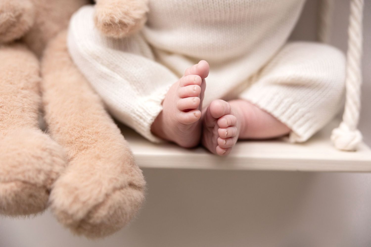 Newborn baby feet and legs against cream colored knit blanket background.