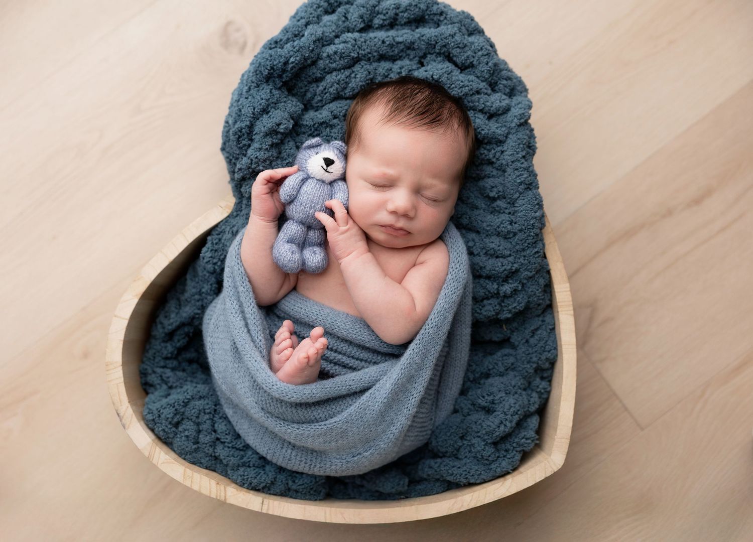 Baby nestled in cozy dark blue knit blanket during professional newborn photoshoot.