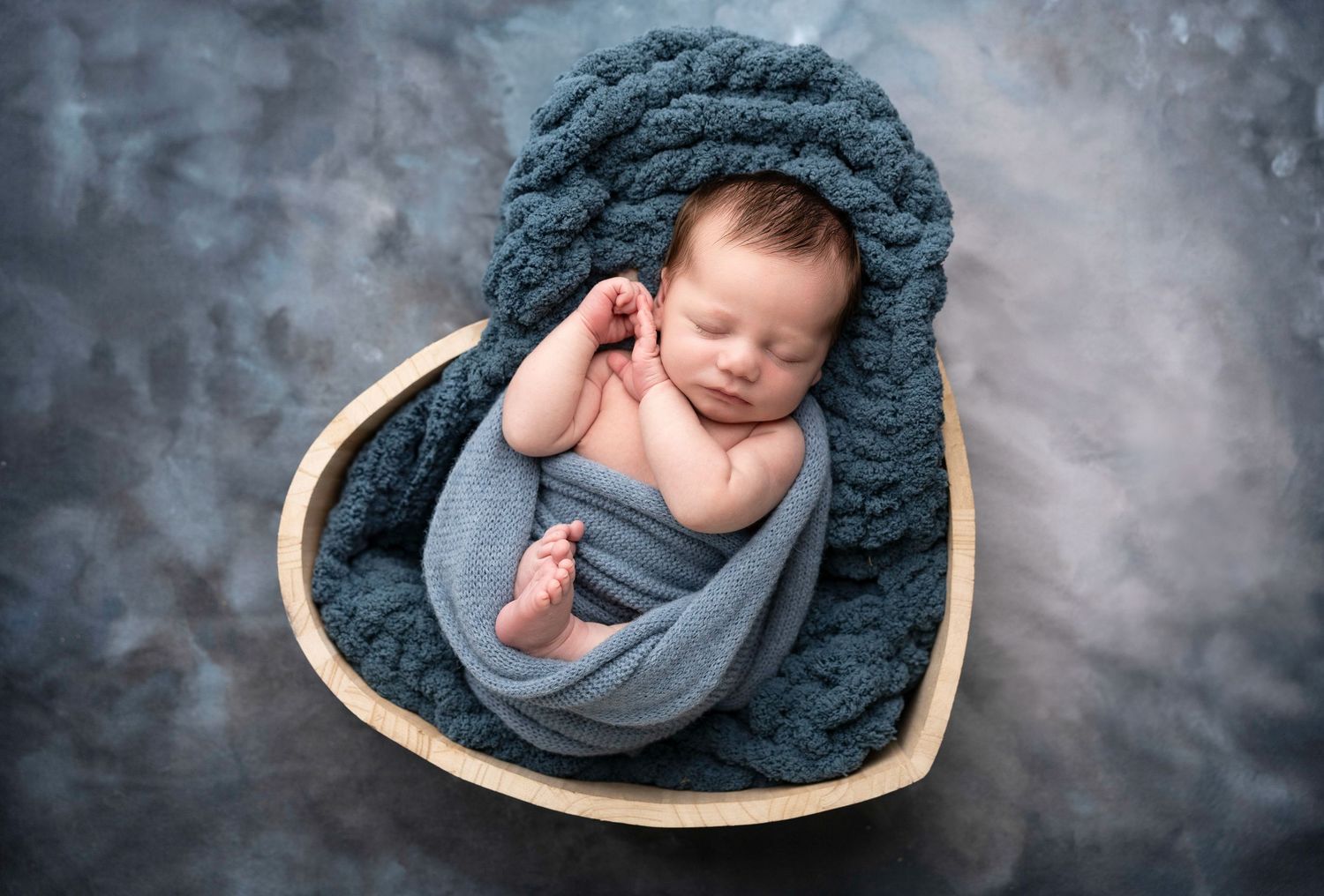 Artistic newborn portrait with moody blue backdrop and dramatic lighting.