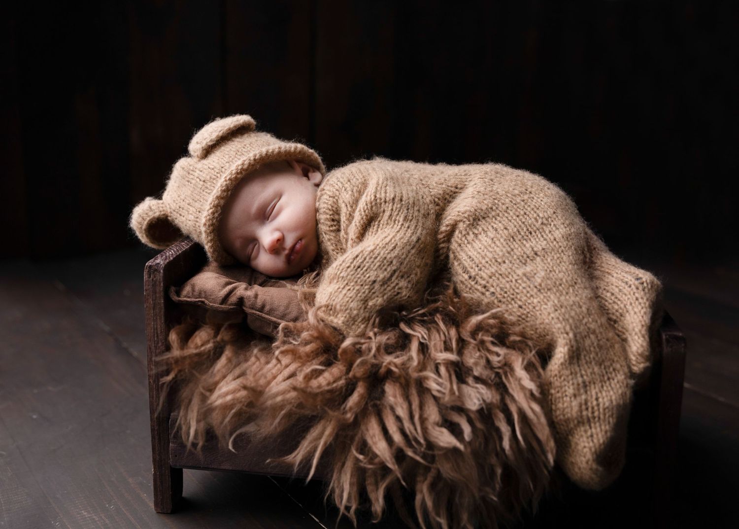 Artistic newborn photography with baby wrapped in brown blanket against dark background.