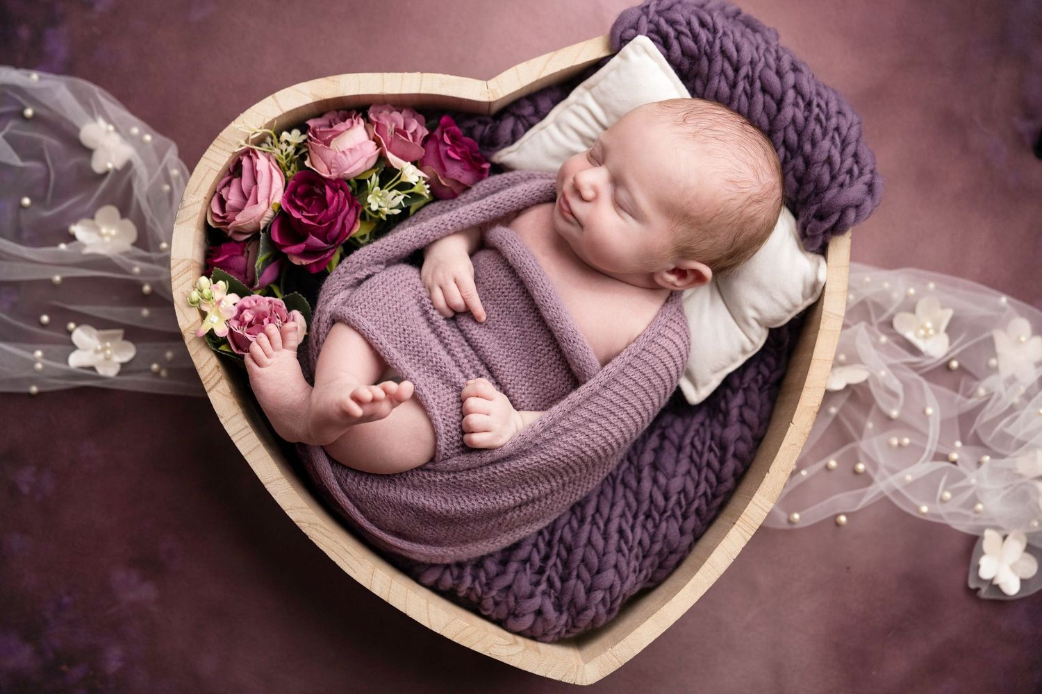 Cozy newborn photography setup with purple wrapping and romantic lighting.