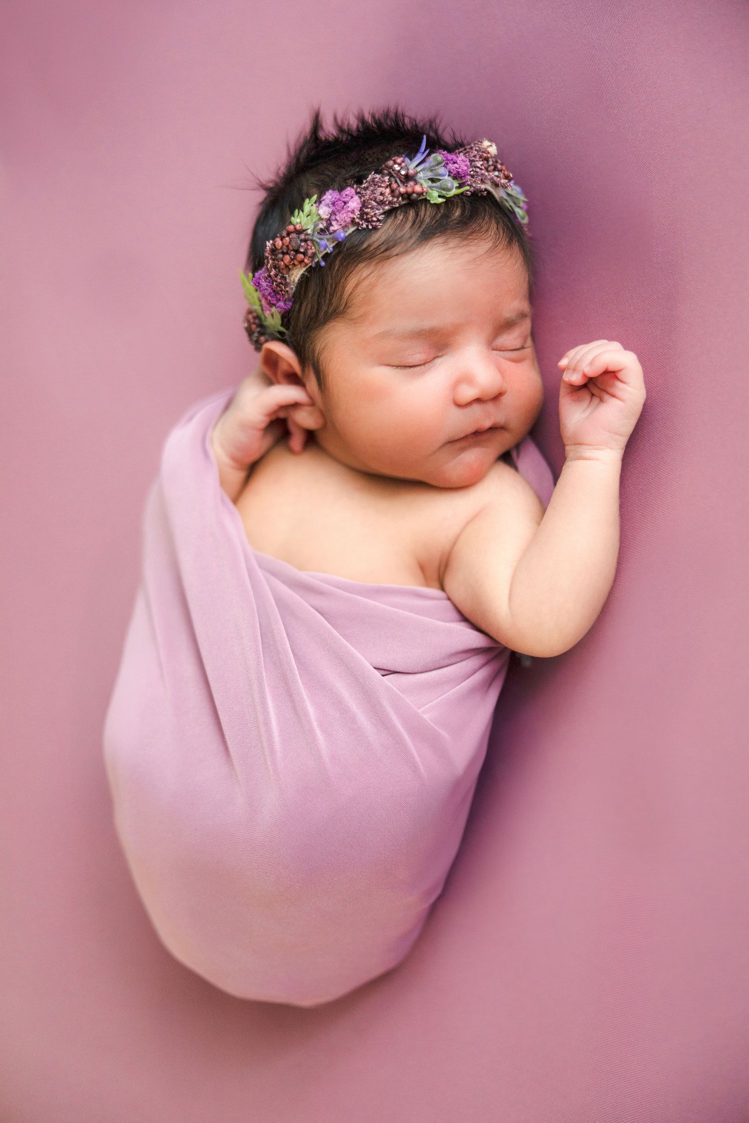 Sleeping newborn wrapped in purple fabric wearing delicate floral headband.