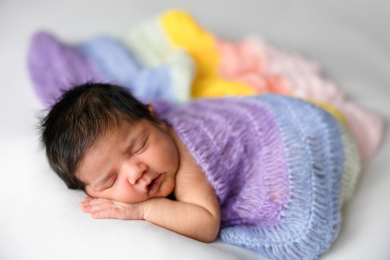 Peaceful newborn sleeping on soft pastel knitted blankets.