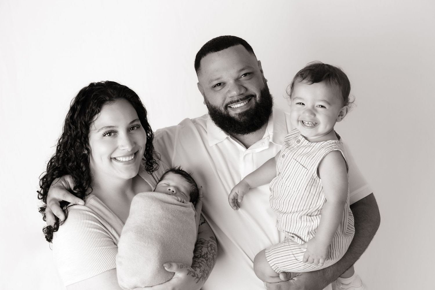 Black and white portrait of family members lying together on white background.