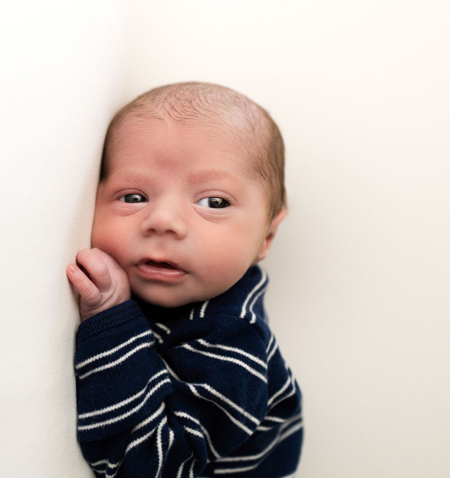 Newborn baby wrapped in navy and white striped blanket against white background.