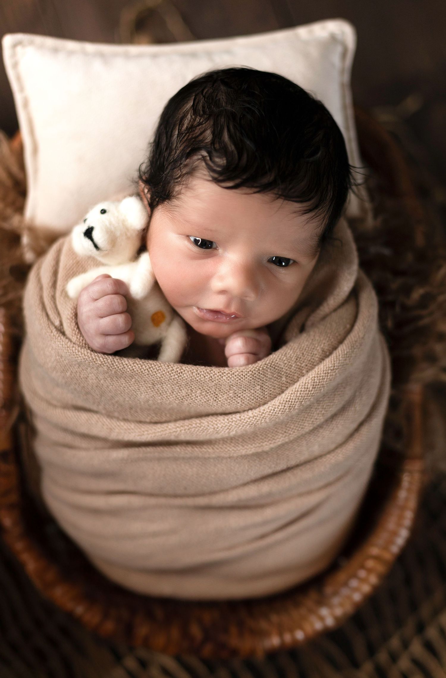 Baby nestled in cozy tan wrap during professional newborn photoshoot.