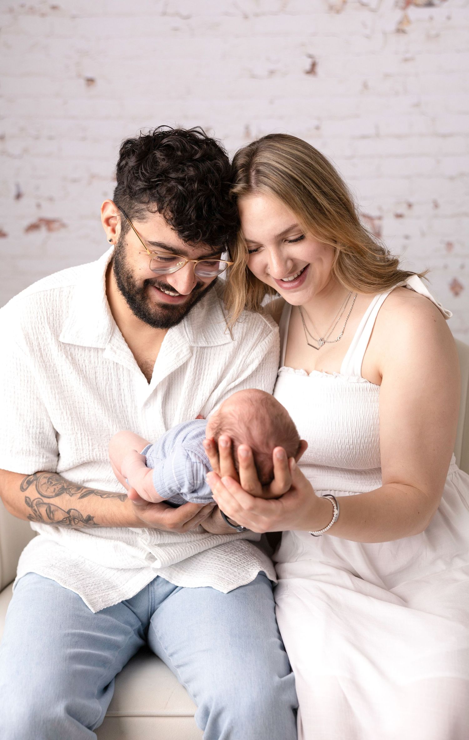 Family photo session with parents in white and denim against brick wall backdrop.