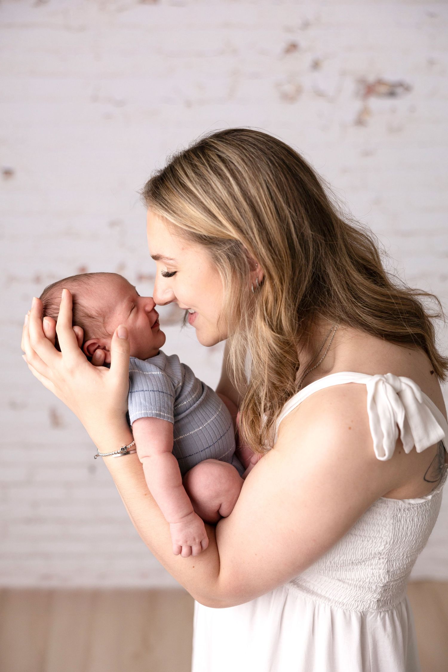 Mother in white dress holding newborn during intimate photo session.