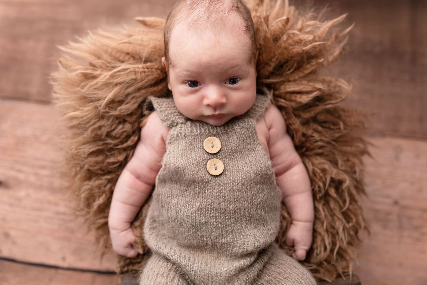 Newborn wearing knit romper posed on brown fluffy backdrop.