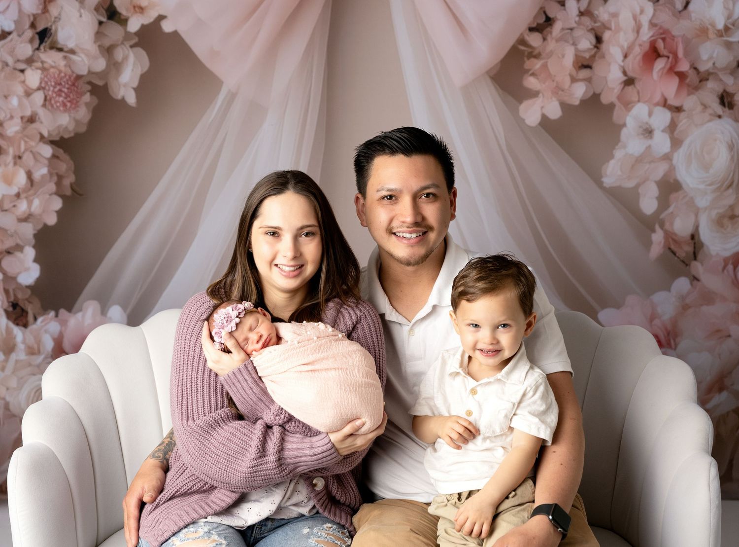Elegant family photo session with pink floral backdrop and white drapery.
