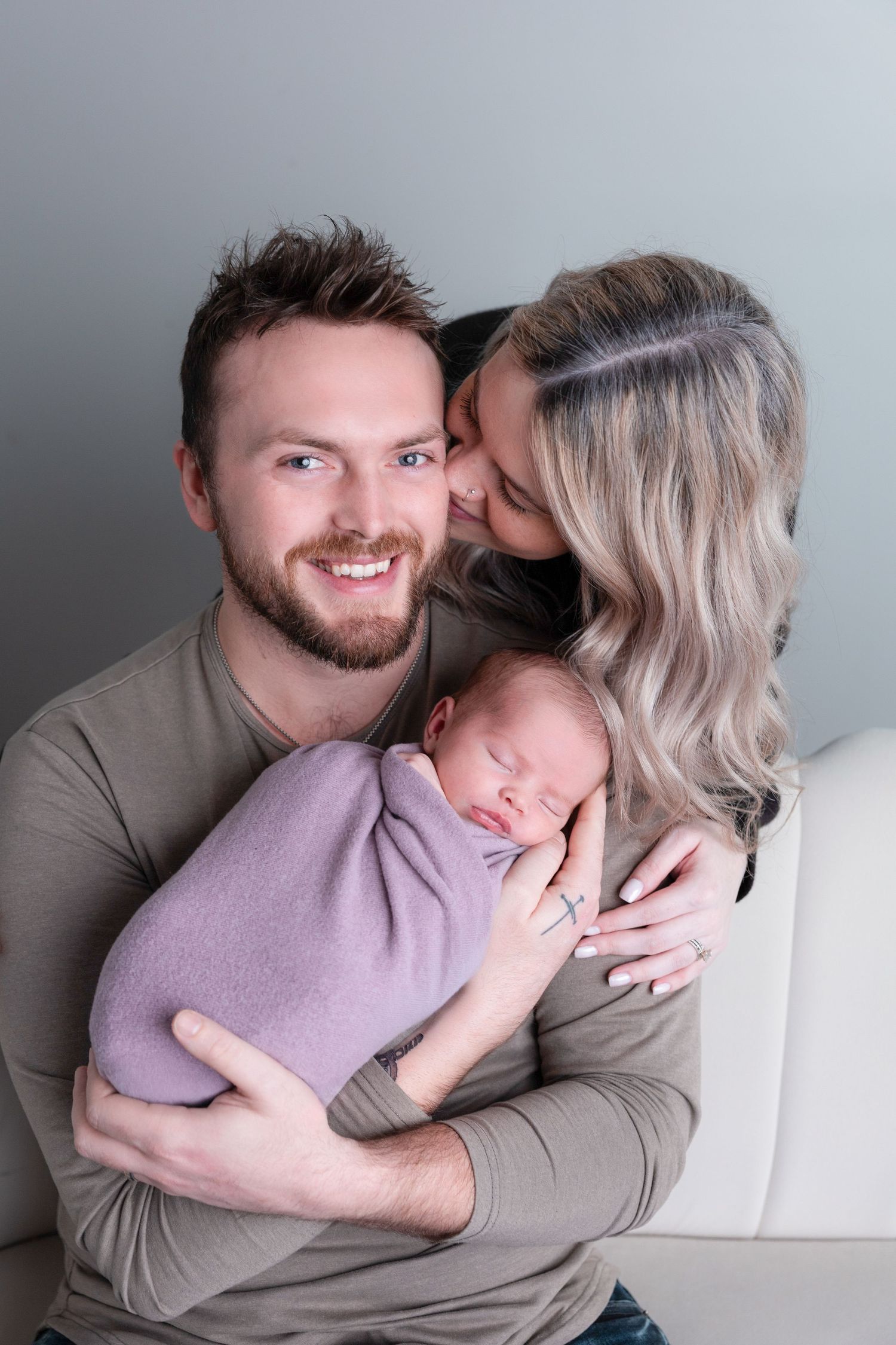 Couple embracing on grey couch during intimate lifestyle photo session.