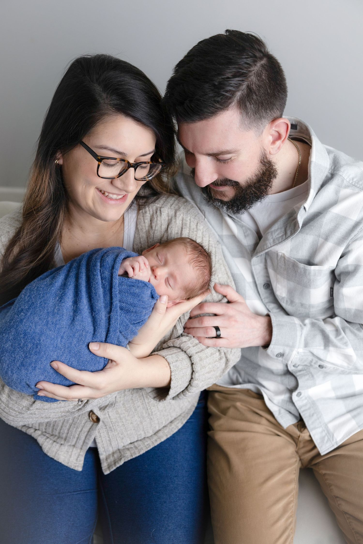 Intimate family portrait series showing parents cuddling with their baby against gray background.