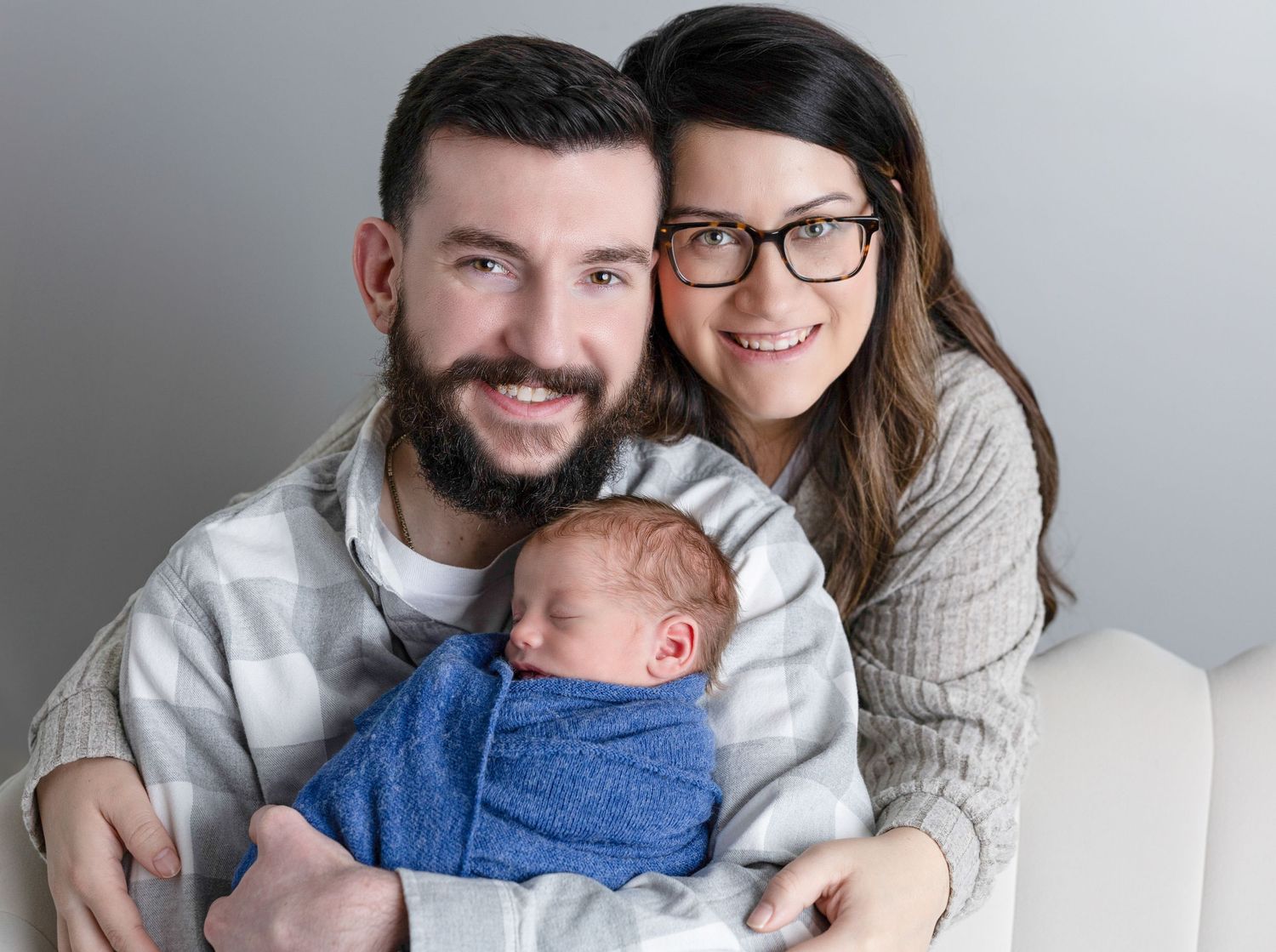 Family of three sharing tender moments together in casual attire against light backdrop.