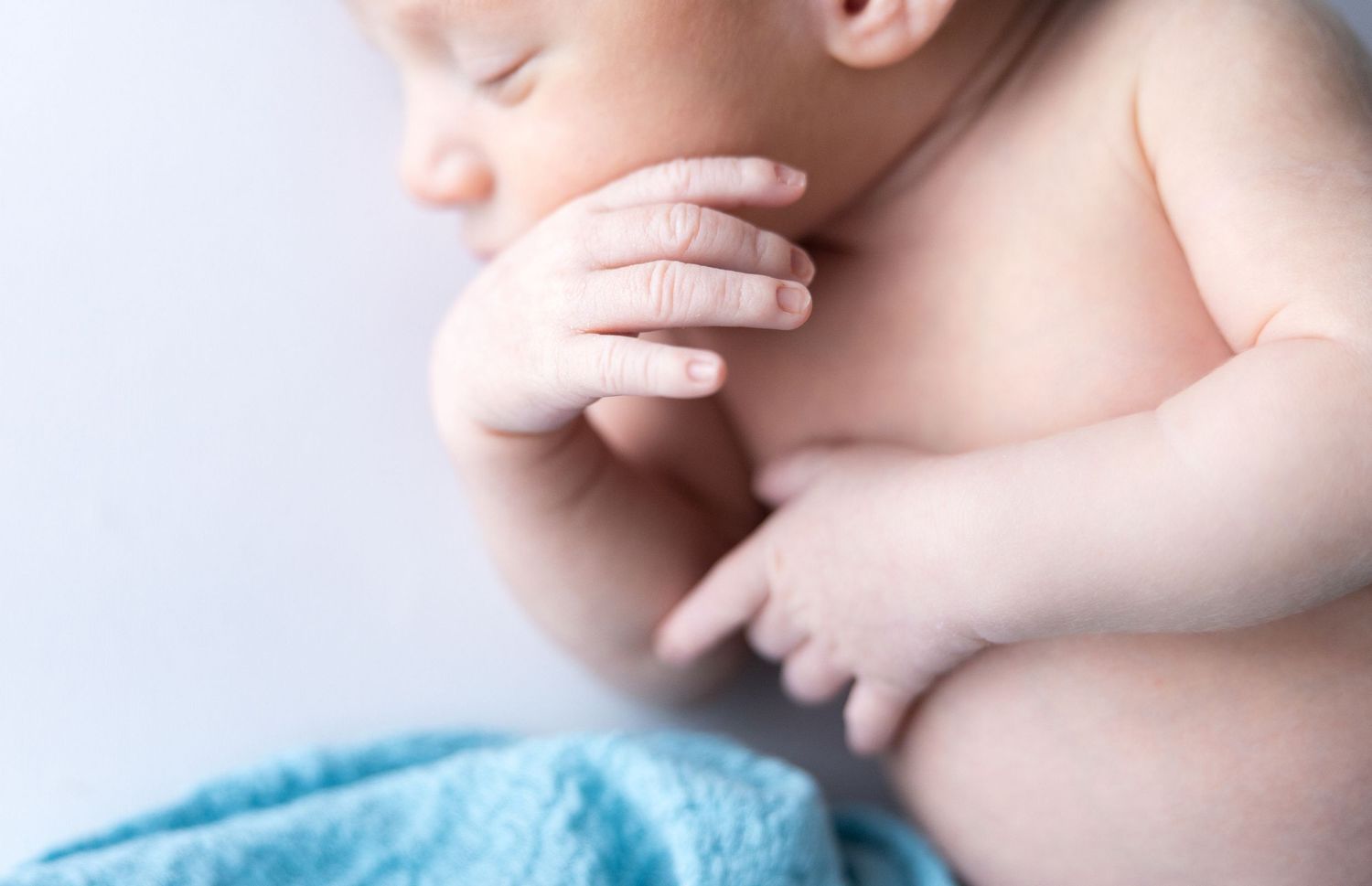 Close-up details of baby's delicate features and skin against soft blue fabric.